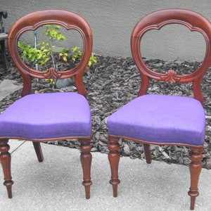 Peut inclure: Deux chaises en bois anciennes avec un rembourrage violet et des dossiers ovales. Les chaises ont des pieds tournés et des détails sculptés.