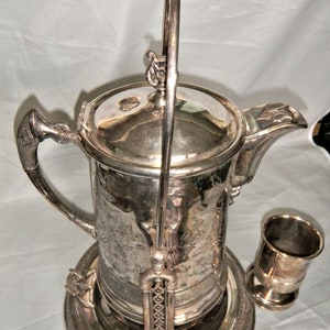 May include: Silver plated ice water jug with a lid, handle, and a removable ice bucket. The jug has an ornate design and is in excellent condition.