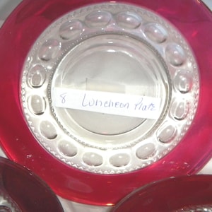 Puede incluir: Un juego de tres platos de almuerzo de vidrio transparente con un borde elevado texturizado y un borde rojo. Los platos están etiquetados como "8 Luncheon Plates".