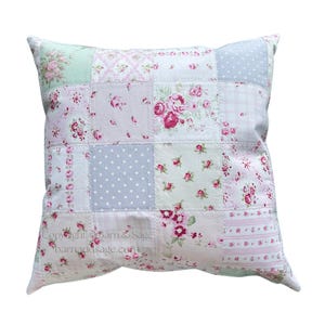 May include: A square throw pillow featuring a patchwork design of various fabric squares in shades of pink, green, white, and grey. The patterns include floral rose prints, polka dots, and plaid stripes. The text Copyright Barn & Sage barnandsage.com is visible.