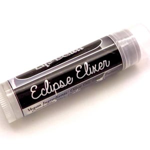 May include: A tube of Eclipse Elixer lip balm with a black label and white text. The label includes the words "lip balm" and "Eclipse Elixer". The lip balm is vegan and lists ingredients like olive oil and shea butter.