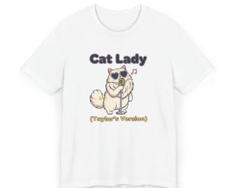 May include: White t-shirt with a cartoon cat wearing heart-shaped sunglasses and holding a microphone. The text "Cat Lady" is above the cat, with "(Taylor's Version)" below. A musical note is also included.