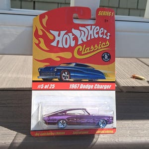 May include: A Hot Wheels Classics Series 1 die-cast 1967 Dodge Charger in purple, packaged on a red and yellow card. The card features the Hot Wheels logo, the text #5 of 25, 1967 Dodge Charger, Die-cast body & chassis, Special paint, and Limited edition.