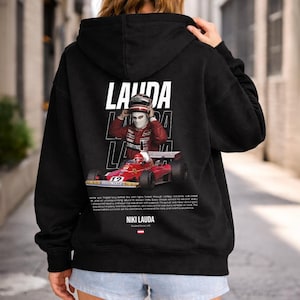 Könnte beinhalten: Schwarzer Kapuzenpullover mit einem Grafikdesign von Niki Lauda, einem Formel-1-Fahrer, und einem roten Rennwagen. Das Design enthält das Wort "Lauda" in weißen Blockbuchstaben.