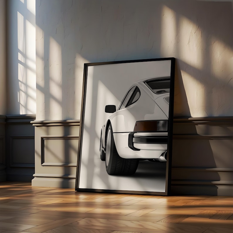 May include: A white classic sports car poster with a black frame. The car is facing away from the camera and the rear of the car is in focus. The poster is leaning against a wall.