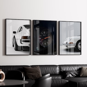 May include: Three black framed prints of white Porsche cars. The center print features a close-up of a car's dashboard with a round gauge that reads "Quarts".