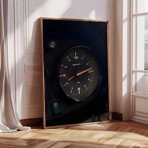 May include: A black and white photograph of a vintage car dashboard with a round clock face. The clock face is black with white numbers and a red hand. The clock face reads "Quartz" and "VDO".