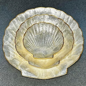 Puede incluir: Juego de tres fuentes decorativas en forma de concha. Las fuentes tienen un acabado nacarado con ribetes dorados. La fuente más grande mide unos 30 cm de diámetro, la mediana 23 cm y la más pequeña 15 cm.