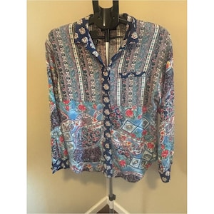 May include: A long-sleeve button-down shirt featuring a multi-colored pattern with vertical stripes on the upper section and a floral and geometric print on the lower section. The shirt has a dark blue collar and a central placket with a floral motif.