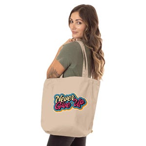 May include: A beige canvas tote bag with adjustable straps. The bag has a colorful graphic design that says "Never Give Up" in a retro style.