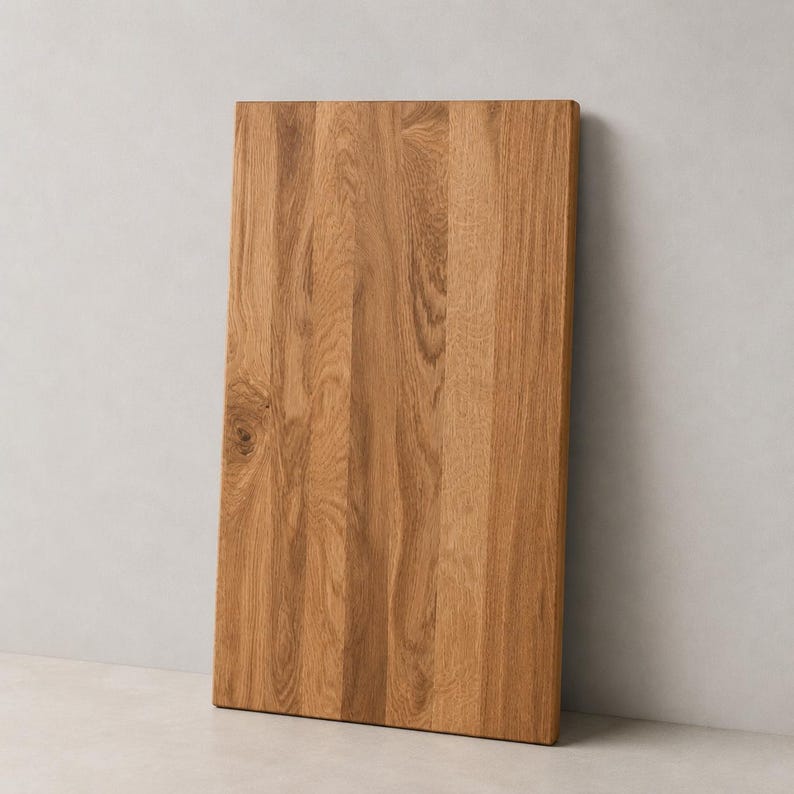 May include: A rectangular wooden cutting board made from light brown oak with a visible natural grain pattern. The board features vertical wood planks joined together, showcasing a smooth surface with a distinct knot on the left side.
