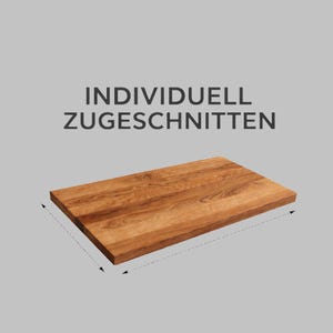 Puede incluir: Una tabla de cortar rectangular de madera con un acabado de vetas naturales. El texto "INDIVIDUELL ZUGESCHNITTEN" está impreso en gris oscuro. La tabla se muestra en ángulo sobre un fondo gris.