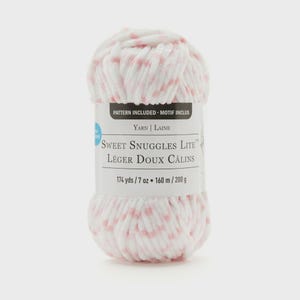 May include: A white and pink speckled yarn ball with the text "Sweet Snuggles Lite" and "174 yds / 7 oz". The yarn is a soft, fluffy texture, perfect for knitting or crocheting projects. The label also says "Pattern Included".