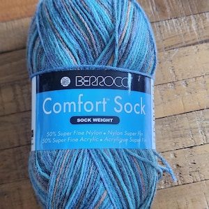 May include: A ball of Berroco Comfort Sock yarn in shades of blue, teal, and brown. The label reads "Comfort Sock" and lists the fiber content as 50% Super Fine Nylon and 50% Super Fine Acrylic.