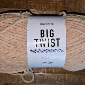 Puede incluir: Ovillo grande de lana beige de la marca Big Twist, 100% poliéster. La etiqueta dice "BIG TWIST". El hilo es de 213 m / 200 g. Ideal para tejer o hacer ganchillo.