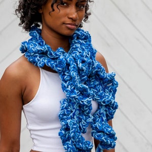 Hand crochet chunky ruffled mixed blues scarf made with strands of varied texture yarns in shades of royal, sapphire and ocean blue. Scarf tied around neck with ruffles and tassels hanging down front past waist.