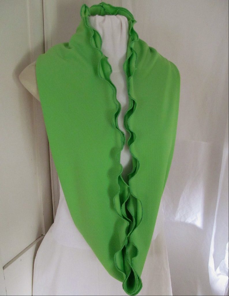 Bright green infinity scarf is folded lengthwise and draped around neck and shoulders of mannequin with ruffles framing the neckline. Lime green knit fabric scarf features kelly green machine stitched ruffled edge. Remiscent of spring lettuce greens.