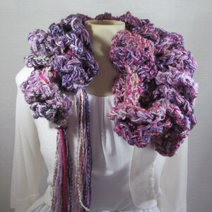 Hand crochet chunky ruffled mixed berry scarf with multiple strands of varied synthetic yarns in shades of purple grape, blueberry and raspberry. This purple scarf is 93 inches long by 6 inches wide. Soft and warm with 15 inch long tassels for tying.