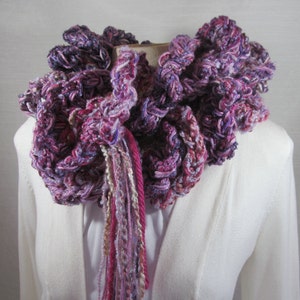 Hand crochet chunky ruffled mixed berry scarf with multiple strands of varied synthetic yarns in shades of purple grape, blueberry and raspberry. This purple scarf is 93 inches long by 6 inches wide. Soft and warm with 15 inch long tassels for tying.