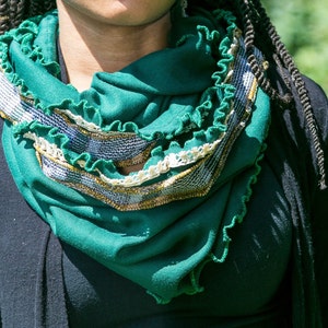 Close view of model with green infinity scarf wrapped twice around neck, highlights the emerald green jersey knit fabric, kelly green stitched ruffled edges, vintage ivory lace and vintage mustard yellow and green plaid fabric trim.