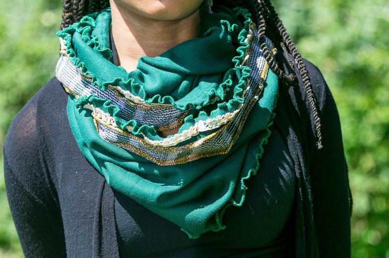 Close view of model with green infinity scarf wrapped twice around neck, highlights the emerald green jersey knit fabric, kelly green stitched ruffled edges, vintage ivory lace and vintage mustard yellow and green plaid fabric trim.