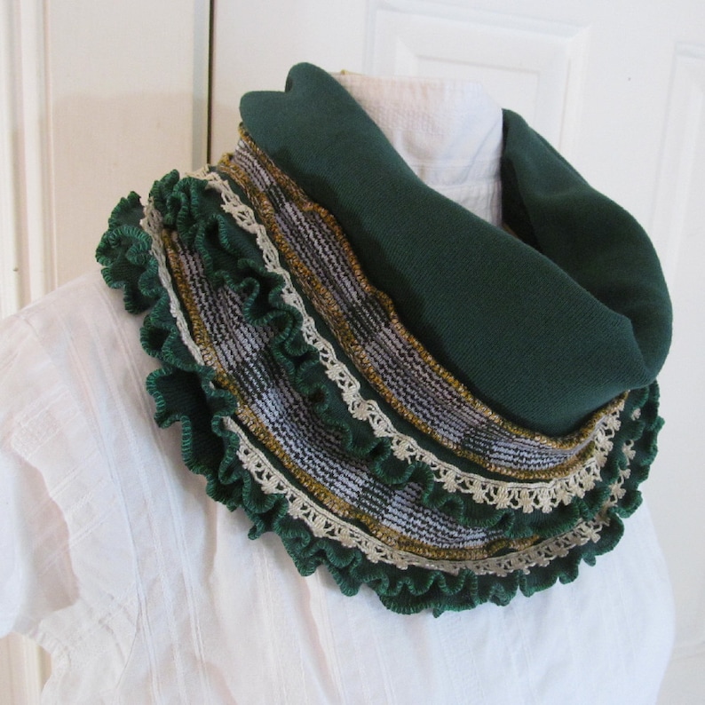 Close view of emerald green infinity scarf wrapped around neck of mannequin shows details of the narrow vintage ivory lace and vintage mustard yellow and green plaid fabric trim stitched near the kelly green stitched ruffled edge of the scarf.