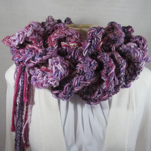 Hand crochet chunky ruffled mixed berry scarf with multiple strands of varied synthetic yarns in shades of purple grape, blueberry and raspberry. This purple scarf is 93 inches long by 6 inches wide. Soft and warm with 15 inch long tassels for tying.