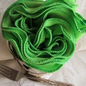 Bright green infinity scarf is folded lengthwise and rolled with ruffles facing up.  Remiscent of spring lettuce, the scarf sits in a silver bowl next to a fork. Lime green knit fabric scarf features kelly green machine stitched ruffled edge.