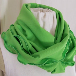 Bright green infinity scarf is folded lengthwise and wrapped double around the neck of mannequin. Lime green knit fabric scarf features kelly green machine stitched ruffled edge. Lovely spring green reminiscent of spring lettuce and greens.