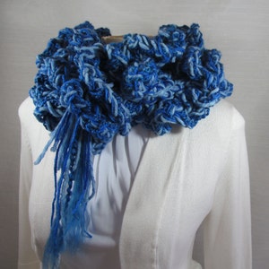 Hand crochet chunky ruffled mixed blues scarf made with strands of varied texture yarns in shades of royal, sapphire and ocean blue. Scarf doubled and looped around neck with tassels through loop and hanging down front. Ruffles fill the neckline.