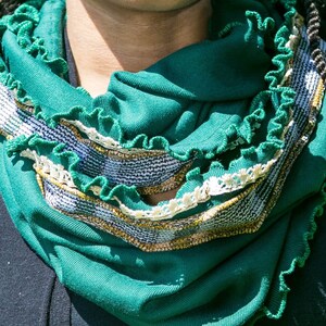 Close view of deep green infinity scarf wrapped twice around neck, highlights the emerald green jersey knit fabric with kelly green stitched ruffled edges, narrow vintage ivory lace and vintage mustard yellow, white and green plaid fabric trim.