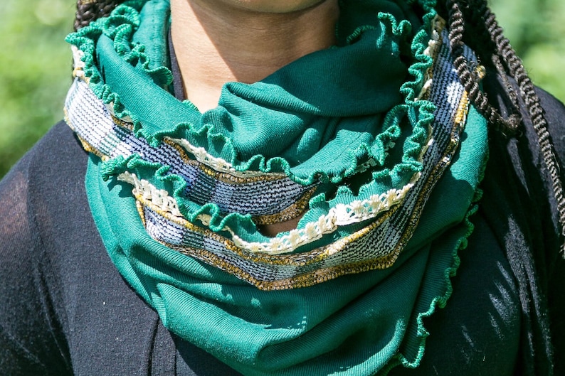 Close view of deep green infinity scarf wrapped twice around neck, highlights the emerald green jersey knit fabric with kelly green stitched ruffled edges, narrow vintage ivory lace and vintage mustard yellow, white and green plaid fabric trim.