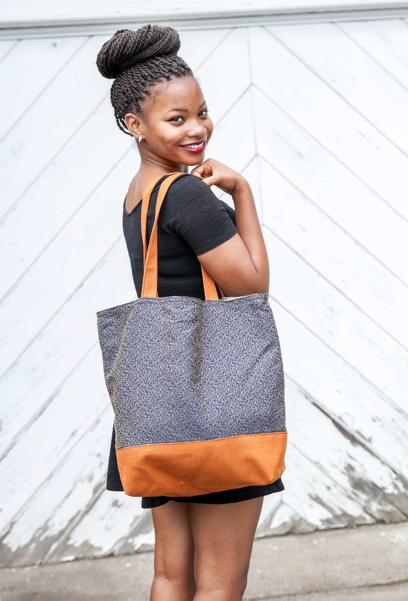 Tote bag main fabric of antique gold flourishes designer upholstery fabric on navy blue background. Straps and bag bottom of rust orange upholstery fabric with small geometric design. Heavy weight cotton duck cloth lining. Carry over shoulder.