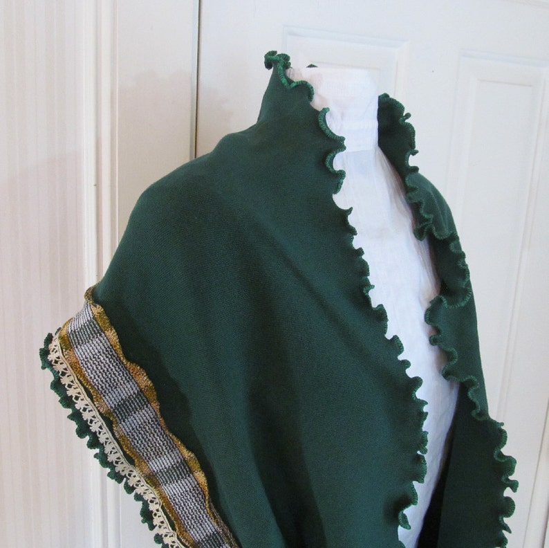 Deep green scarf draped over shoulders of mannequin as a shawl. Kelly green ruffled edge around neck. The other edge has narrow vintage ivory lace and vintage mustard yellow and green plaid fabric trim stitched near the kelly green ruffled edge.