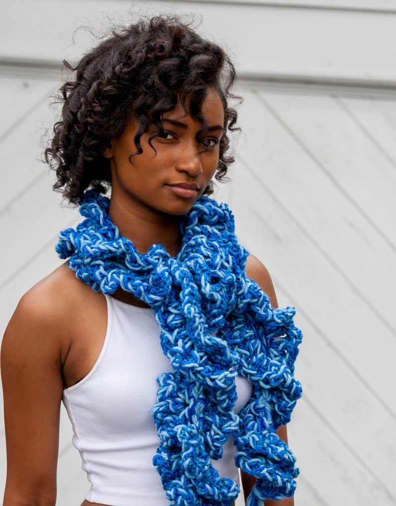 Hand crochet chunky ruffled mixed blues scarf made with strands of varied texture yarns in shades of royal, sapphire and ocean blue. Scarf tied around neck with ruffles and tassels hanging down front past waist.