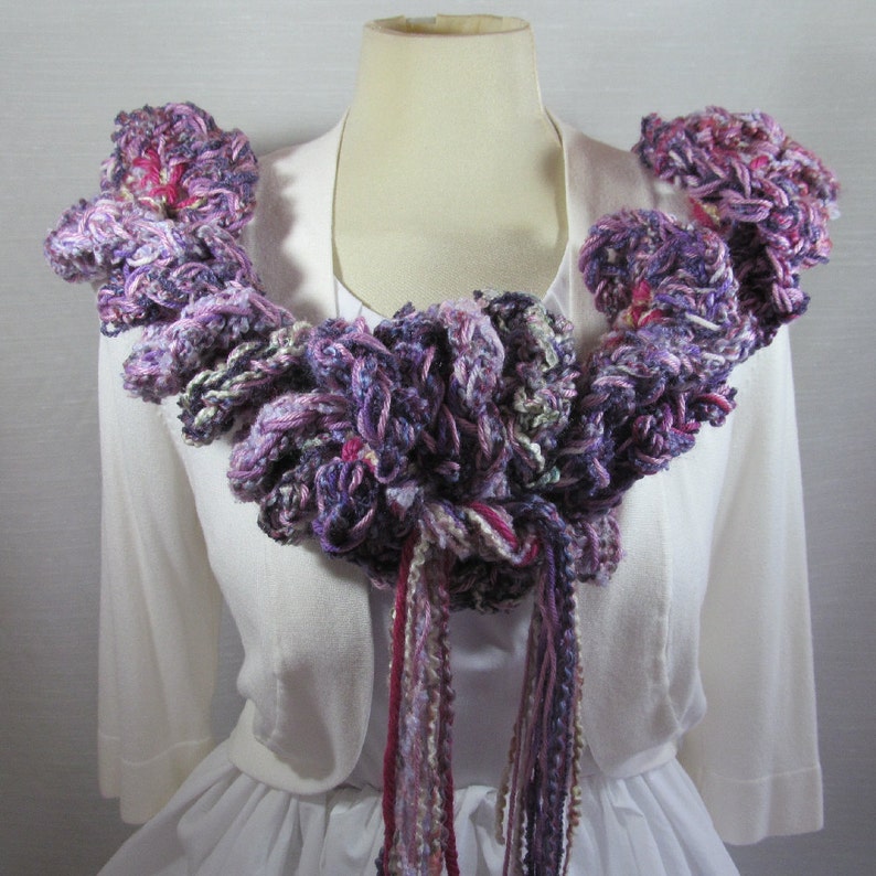 Hand crochet chunky ruffled mixed berry scarf with multiple strands of varied synthetic yarns in shades of purple grape, blueberry and raspberry. This purple scarf is 93 inches long by 6 inches wide. Soft and warm with 15 inch long tassels for tying.