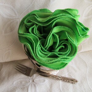 Bright green infinity scarf is folded lengthwise, rolled with ruffles facing up in a silver bowl, remiscent of spring lettuce greens. Lime green knit fabric scarf features kelly green machine stitched ruffled edge.