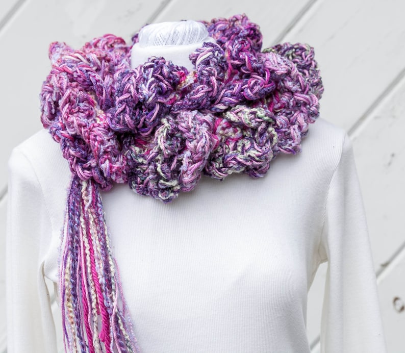 Hand crochet chunky ruffled mixed berry scarf with multiple strands of varied synthetic yarns in shades of purple grape, blueberry and raspberry. This purple scarf is 93 inches long by 6 inches wide. Soft and warm with 15 inch long tassel for tying.