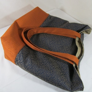 Tote bag main fabric of antique gold flourishes designer upholstery fabric on navy blue background. Straps and bag bottom of rust orange designer upholstery fabric with small geometric design in navy. Heavy weight cotton duck cloth lining.