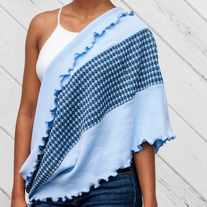 May include: A light blue shawl with a patterned center panel. The shawl has a wavy, ruffled edge and is draped over the shoulders. The center panel features a blue and white geometric design.