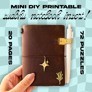 May include: A brown leather notebook with a gold star charm and a white pen secured by a gold pen holder. The notebook insert is labeled "Mini DIY Printable Sudoku Notebook Insert!" with 20 pages and 72 puzzles.