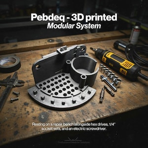 May include: A 3D-printed modular system in black, resting on a wooden repair bench. The system includes a perforated base, a cylindrical component, and other parts. Alongside are hex drives, socket sets, and an electric screwdriver. The text on the image says "Pebdeq - 3D printed Modular System."