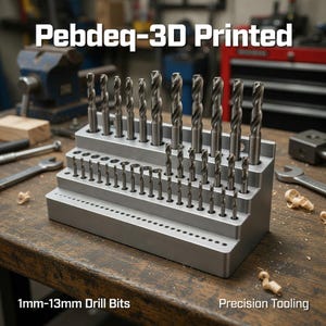 May include: A 3D-printed, silver drill bit organizer holding multiple drill bits. The text "Pebdeq-3D Printed" is at the top. The text "1mm-13mm Drill Bits" is at the bottom. The text "Precision Tooling" is also at the bottom.