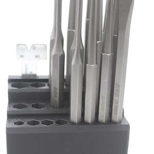May include: A set of metal punches in a black holder. The punches are various sizes and shapes, with a silver finish. The holder has multiple hexagonal holes to store the tools. Some punches have text on them.