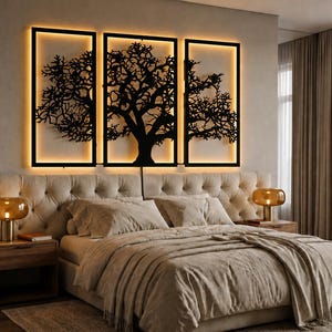 May include: A bedroom scene featuring a large bed with a tufted headboard and matching bedding. Above the bed, three black framed wall art pieces with a tree silhouette design are illuminated with warm lighting. Two bedside tables with lamps complete the scene.