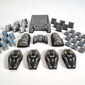 May include: A selection of grey and black game pieces, including numbered shields, computer terminals, and engine components. The set also features small square pieces and circular components with blue and red accents. The pieces are arranged on a white surface.