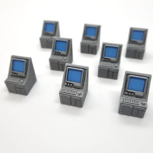 Può includere: Una collezione di modelli di computer grigi in miniatura con schermi blu. Ogni modello ha una tastiera e un piccolo schermo, che assomigliano a computer desktop vintage. Gli oggetti sono disposti su una superficie bianca.
