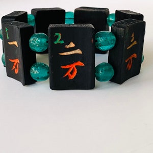 May include: A black bracelet with turquoise beads and black tiles with Chinese characters. The tiles have red and orange painted characters.