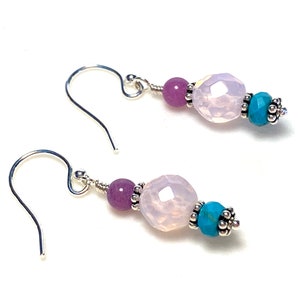 May include: A pair of silver earrings with three beads each. The beads are a light purple, a clear pink, and a turquoise blue.