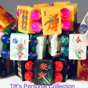 Puede incluir: Una colecci&oacute;n de pulseras hechas con fichas de mahjong vintage en varios colores, incluyendo amarillo, blanco y negro, con s&iacute;mbolos y caracteres grabados, conectadas por cuentas redondas de colores. El texto Tiff's Personal Collection es visible.